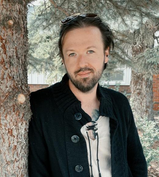 A man standing by a tree wearing a black shirt