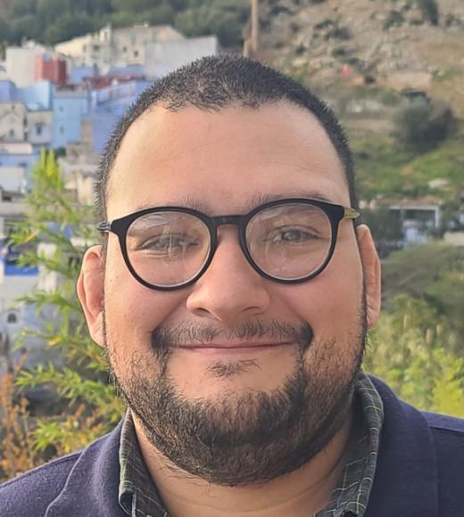 Smiling bearded man with glasses outdoors, colorful hillside houses behind