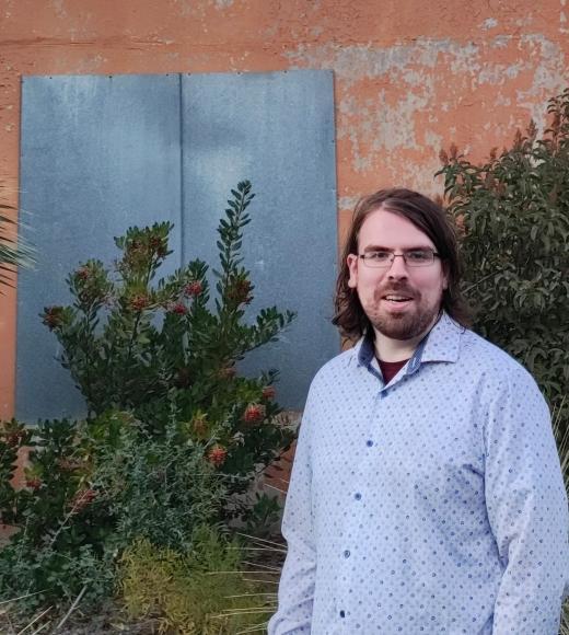 bearded man in front of bushes and panel