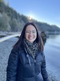 A photo of a woman in a jacket by a river and forest