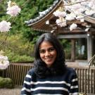 Smiling woman in striped sweater among pink cherry blossoms by a wooden temple pavilion