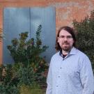 bearded man in front of bushes and panel