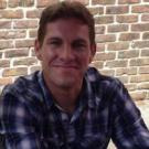 a man wearing plaid in front of a brick wall